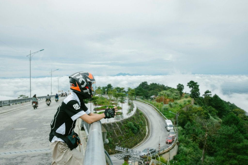 A man on a motorcycle looking over the edge of a bridge